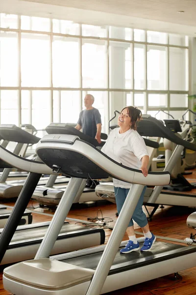 Mujer mayor feliz en auriculares haciendo ejercicio en el gimnasio. — Foto de Stock