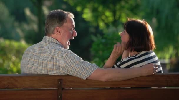 Szczęśliwa para seniorów śmiejąca się i żartująca na ławce w parku. — Wideo stockowe