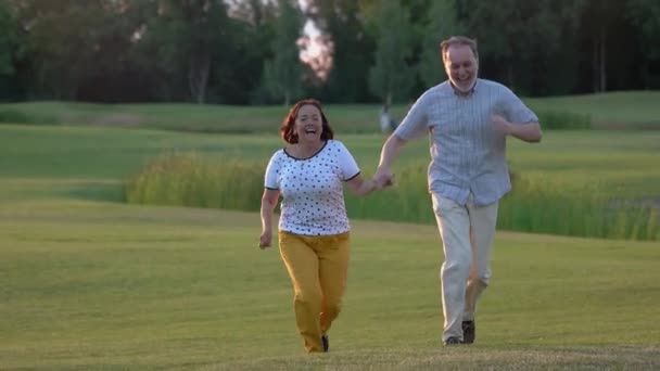 Retired couple running and having fun on green grass. — Stock Video