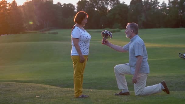 Senior man on knee giving flowers to his woman outdoors. — Stock Video