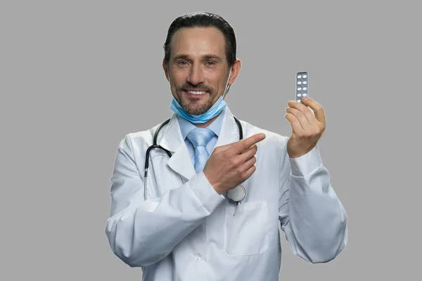 Male caucasian doctor showing pills on gray background. — Stock Photo, Image