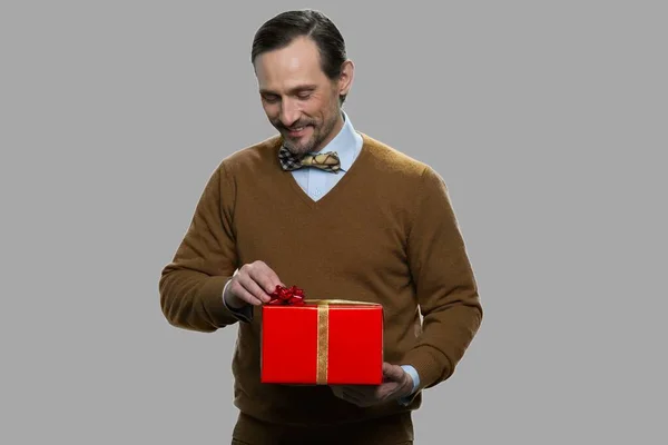 Schöner Mann mit Geschenkbox auf grauem Hintergrund. — Stockfoto