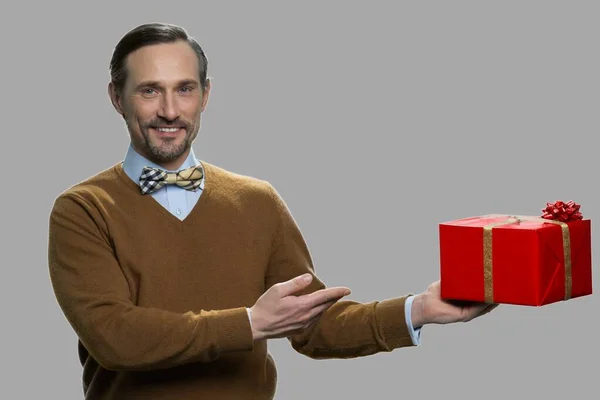 Handsome man showing gift box against gray background. — Stock Photo, Image