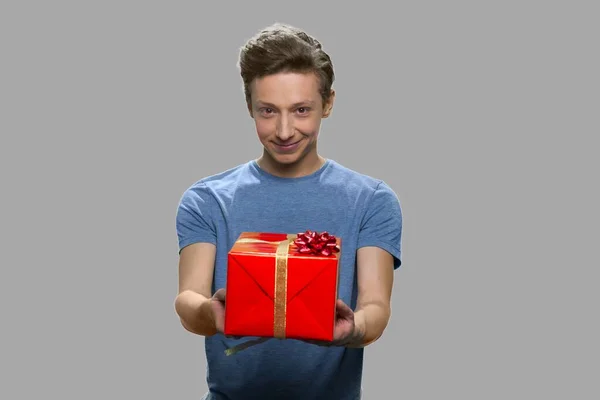 Handsome teen boy offering gift box to someone. — Stock Photo, Image
