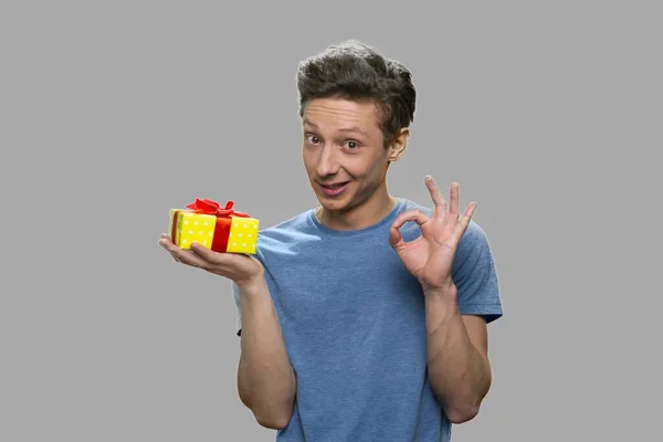Teenage fiú bemutató ajándék doboz és oké gesztus. — Stock Fotó