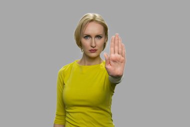 Gri arka planda dur hareketi gösteren genç bir kadın.