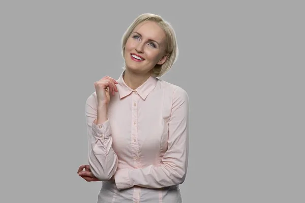 Mujer de negocios sonriente soñando despierto sobre fondo gris. — Foto de Stock