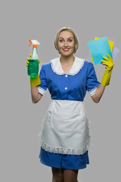 Feliz empregada surpresa em uniforme segurando trapos e detergente. — Fotografia de Stock