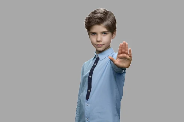 Liten pojke visar stopp gest på grå bakgrund. — Stockfoto