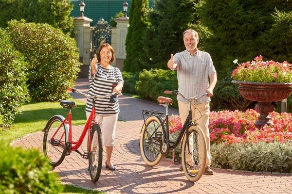 Volwassen paar met fietsen tonen duimen omhoog. — Stockfoto