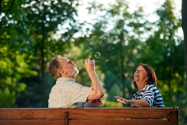 Pareja jubilada soplando burbujas de jabón al aire libre. — Foto de Stock