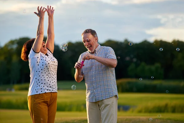 Щасливий зрілий чоловік і жінка дме бульбашки на відкритому повітрі . — стокове фото