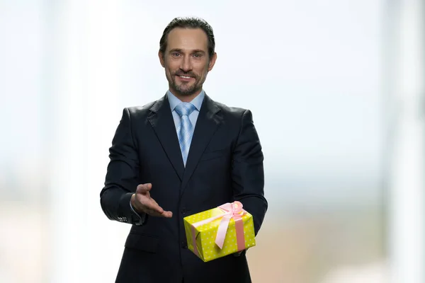 Χαμογελώντας θετικός επιχειρηματίας παρουσιάζει κίτρινο κουτί δώρου. — Φωτογραφία Αρχείου