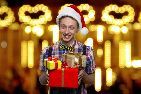 Fröhlicher Teenager mit Weihnachtsmütze hält Geschenkboxen in der Hand. — Stockfoto