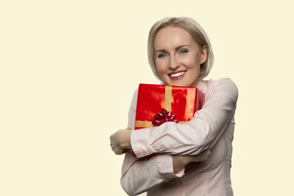 Felice donna matura sta abbracciando una scatola regalo rossa. — Foto Stock