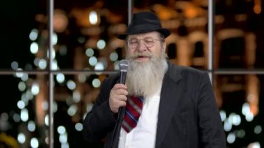 Takım elbiseli neşeli adam mikrofona konuşuyor..