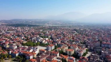 Dağların arka planındaki kırmızı çatılı binaların üzerindeki hava manzarası.