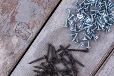 Ahşap arka planda siyah ve gümüş vidalar yığını.