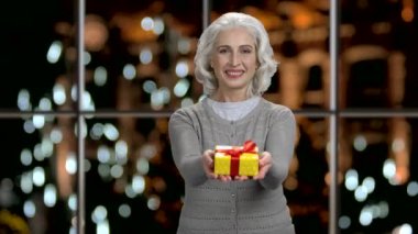 Happy senior woman giving gift box to camera.