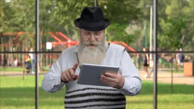 Senior bearded man using digital tablet outdoor.