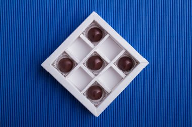 Five brown chocolate candies in the box on blue background.
