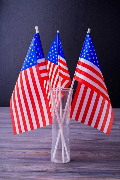 Vertical shot vase of three US flags on grey wooden desk background.