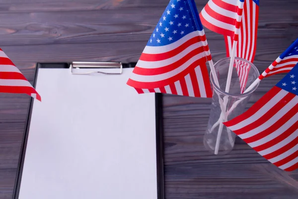 Top view clipboard with blank paper and US flags on grey wood. — Stockfoto