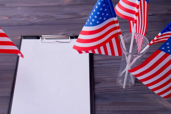 Top view clipboard with blank paper and US flags on grey wood. — Stock fotografie