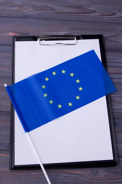 Blank clipboard and blue EU flag on grey wooden desk. — Photo