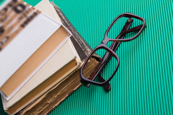 Stack of old books and eyeglasses frame on green background. — Stockfoto