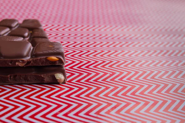 Close-up cut chocolate bar pieces with nuts on red and white background. — Fotografia de Stock