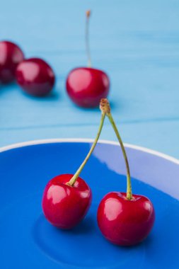 Mavi tabakta dikey yakın plan kırmızı kirazlar..