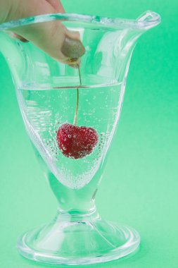 Yakın plan kadın eli bir bardak suya kiraz koyar..