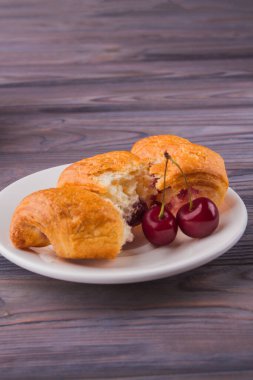 Kruvasan parçaları ve ahşap zemin üzerinde taze kırmızı kirazlar..