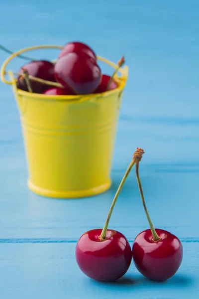 Pequeno balde amarelo cheio de cerejas vermelhas frescas. — Fotografia de Stock