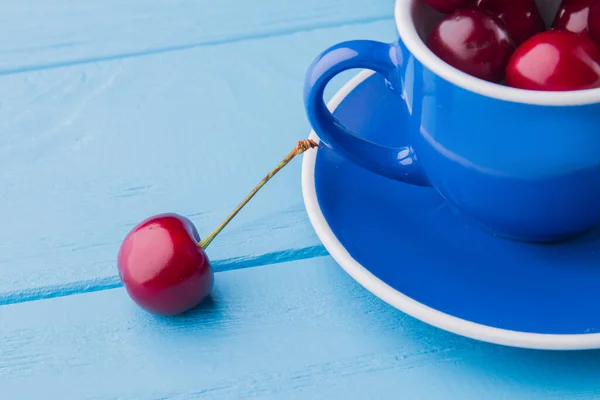 Cerise brillante et tasse bleue sur la surface du bureau en bois. — Photo