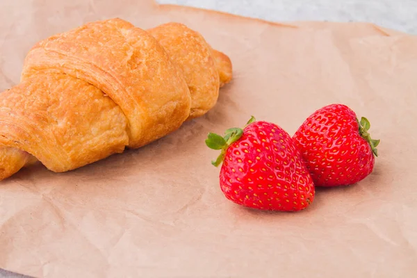 Närbild croissant och två färska råa röda jordgubbar. — Stockfoto