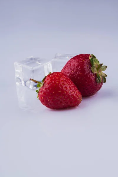Dvě čerstvé syrové červené jahody a kostky ledu izolované na bílém. — Stock fotografie
