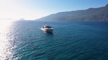 Deniz koyunda yüzen turistlerle bir yat gezisi. Arka planda güzel yeşil dağlar.