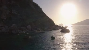 Okyanus ve kayalık sahilde gün batımı. Kıyıda turistli tekneler.