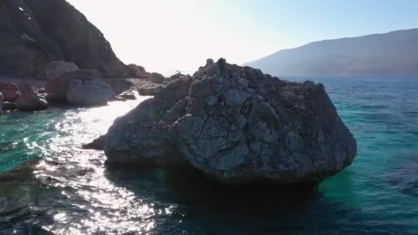 Kamień w wodzie morskiej. Widok na skalisty brzeg, fale morskie i góry. — Wideo stockowe