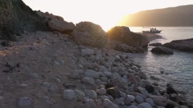 Kayalık kıyı manzarası ve sakin deniz günbatımı altındaki dağlar..