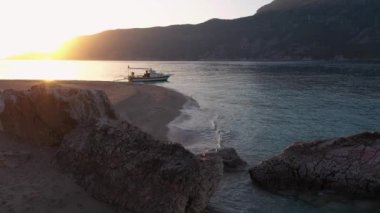 Sakin deniz dalgaları, gün batımında tekne ve dağların olduğu vahşi sahil manzarası..