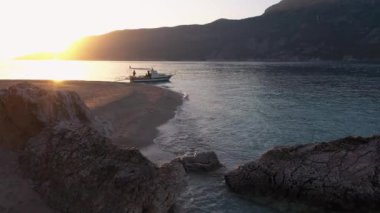 Gün batımında vahşi tropik ada sahili manzarası. Sahilde arka planda dağlar olan bir tekne..