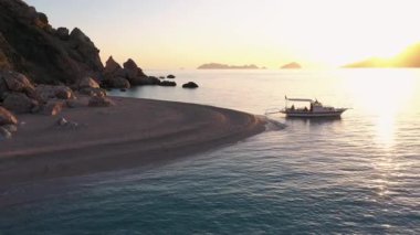 Vahşi kayalık plajı ve gün batımında park edilmiş bir tekne. Güzel deniz manzarası.