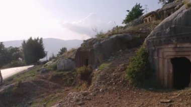 Asfalt yolun yakınındaki dağ yamacında oyulmuş kadim mezarların görüntüsü.