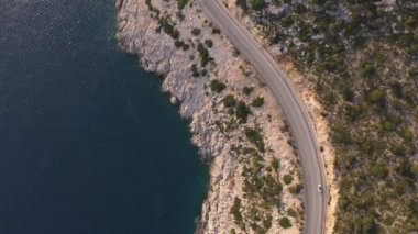 Yaz aylarında turkuaz deniz kenarındaki dağ yolunun insansız hava aracı görüntüsü.