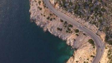 Kuşlar mavi denizin üzerinde giden arabalarla asfalt dağ yolunu görüyorlar..