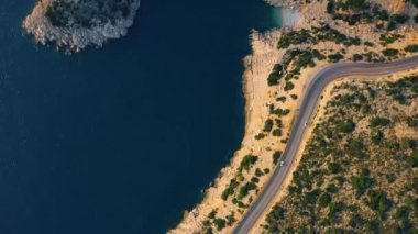 Mavi deniz, kayalık sahil ve asfalt dağ yolu..