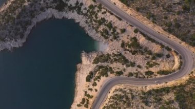 Deniz ve dağlar boyunca kıvrımlı asfalt yolun hava aracı görüntüsü.
